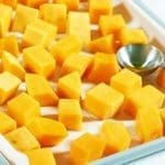 Fresh cut butternut squash covered in olive oil and spread out on a silver cookie sheet