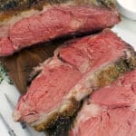 A sliced reverse sear prime rib on a brown wood cutting board.