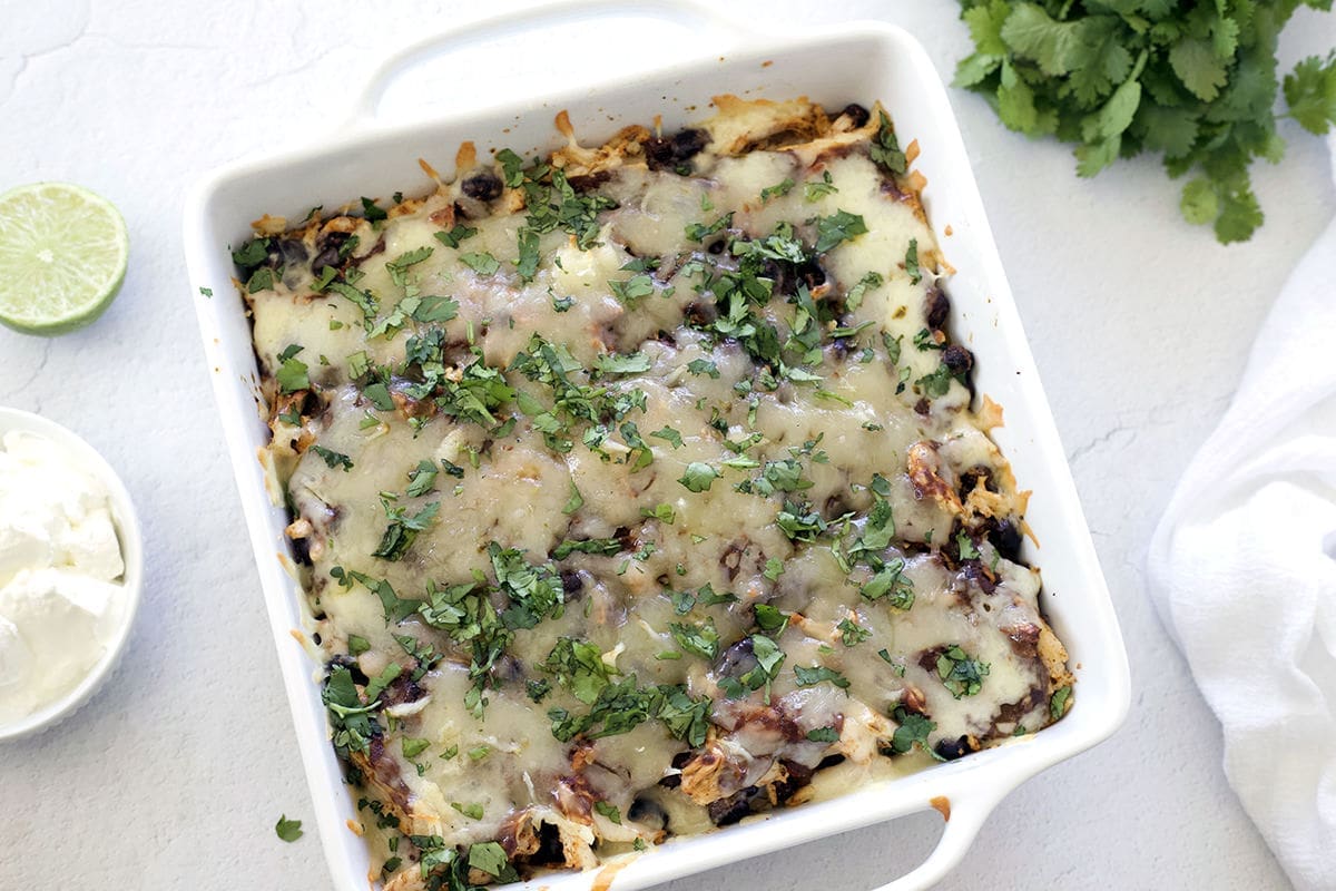 Baked Enchilada Casserole in a white baking dish topped with guacamole and sour cream.