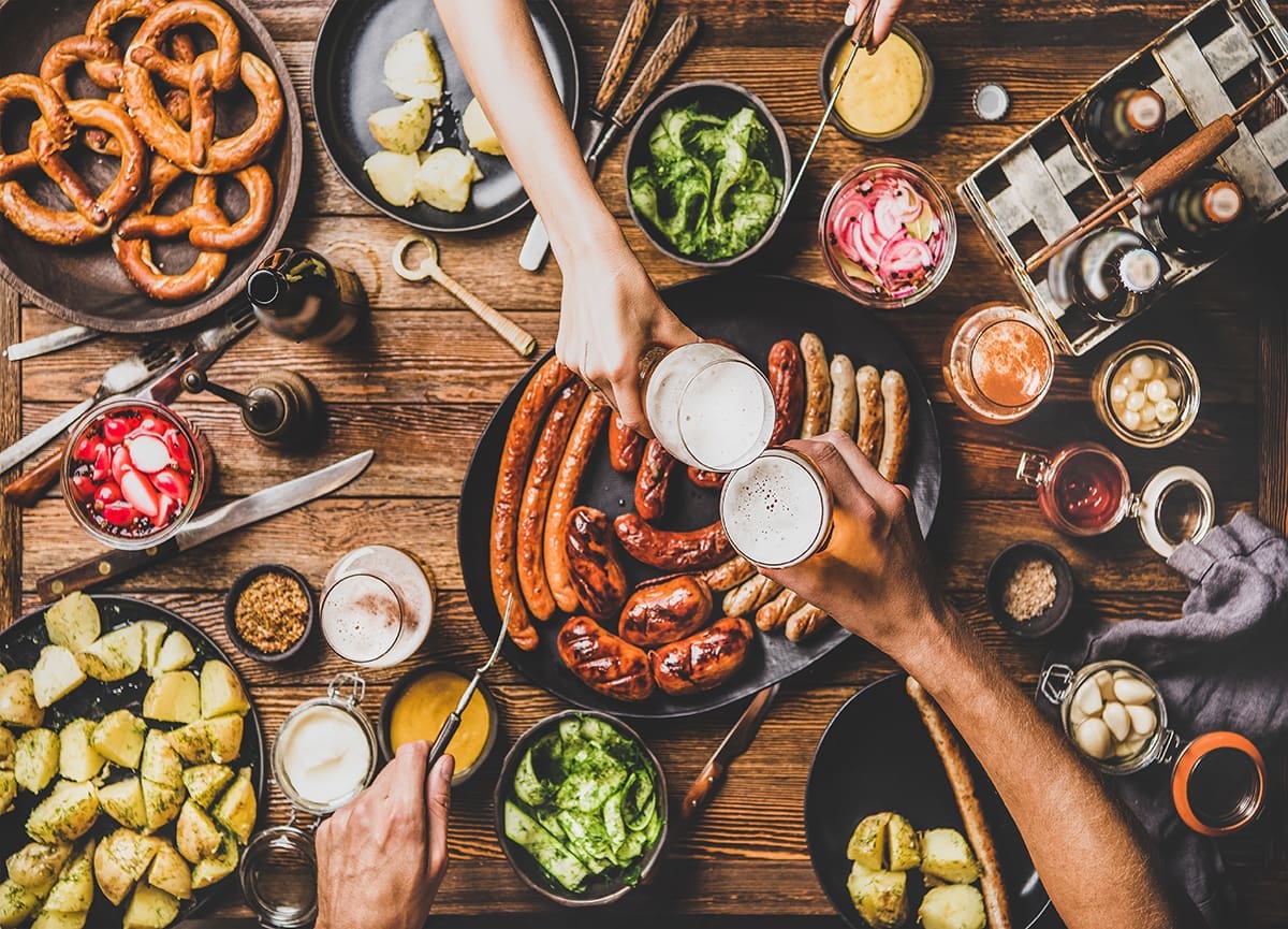German food on a table with folks cheering with beers.