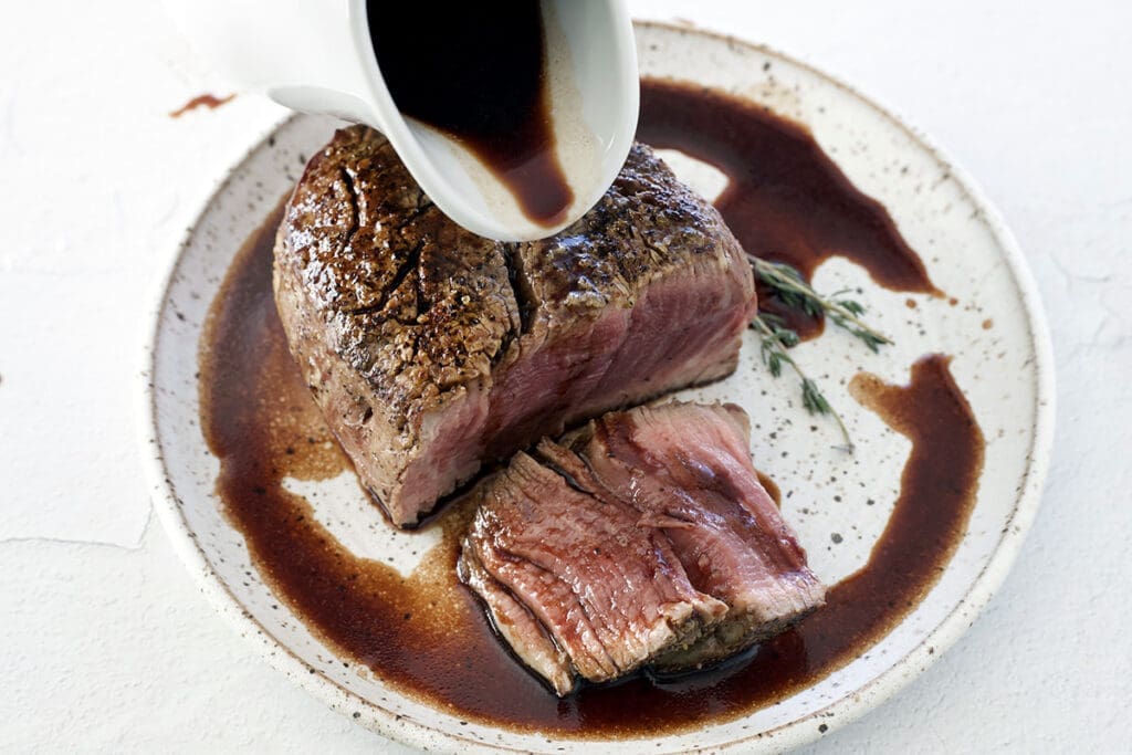 Red Wine Steak Sauce being poured over a baked filet mignon.