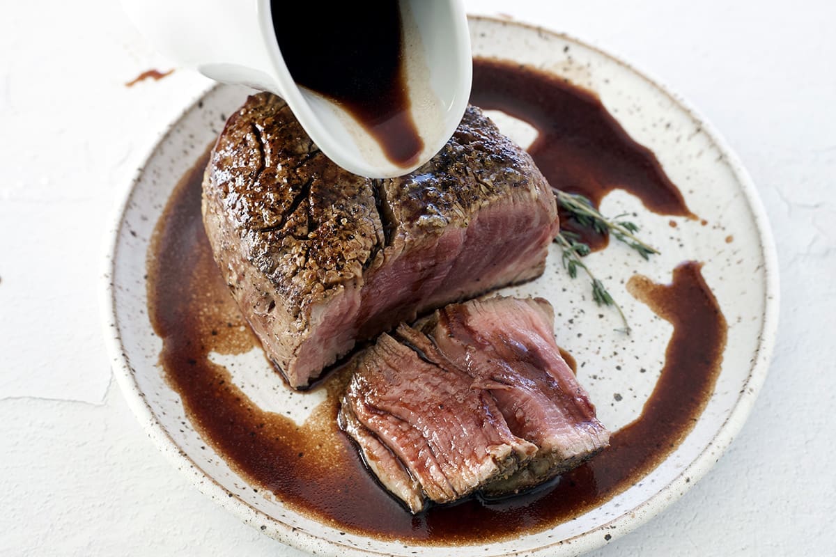 Red Wine Steak Sauce being poured over a baked filet mignon.