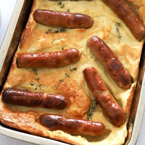 Pan of Toad in a Hole next to a gravy boat full of onion gravy.