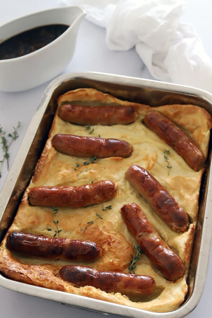 Pan of Toad in a Hole next to a gravy boat full of onion gravy.