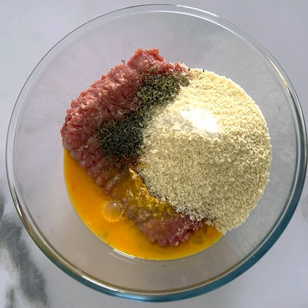 Ground pork, breadcrumbs, egg and herbs in a bowl for sausage roll filling.