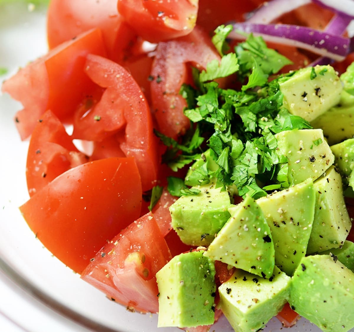 Diced avocados and tomatoes in a clear bowl.