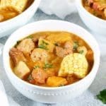 3 bowls of SANCOCHO DOMINICANO in white bowls with a side of cilantro leaves.