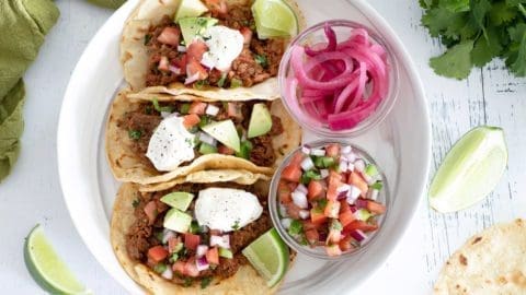 3 steak picado tacos on a white plate with topping options.