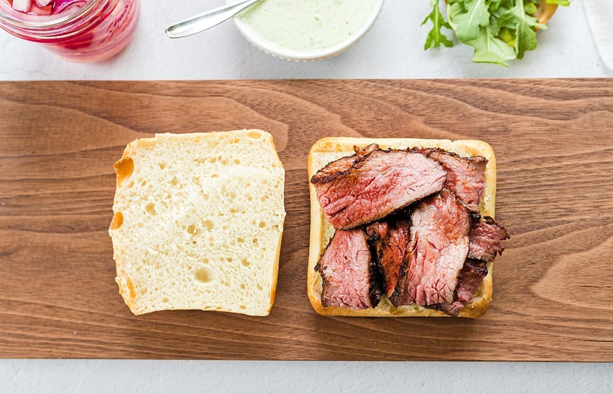 Two cut pieces of bread with cut meat on a cutting board.
