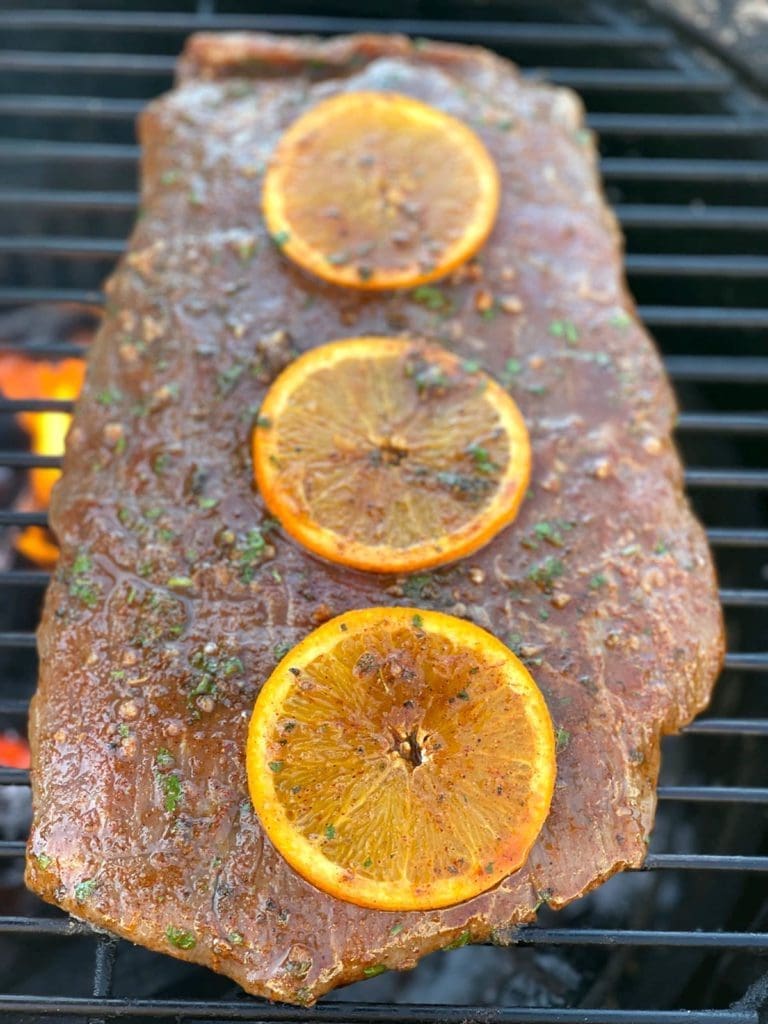 flank steak on the grill with sliced oranges on top.
