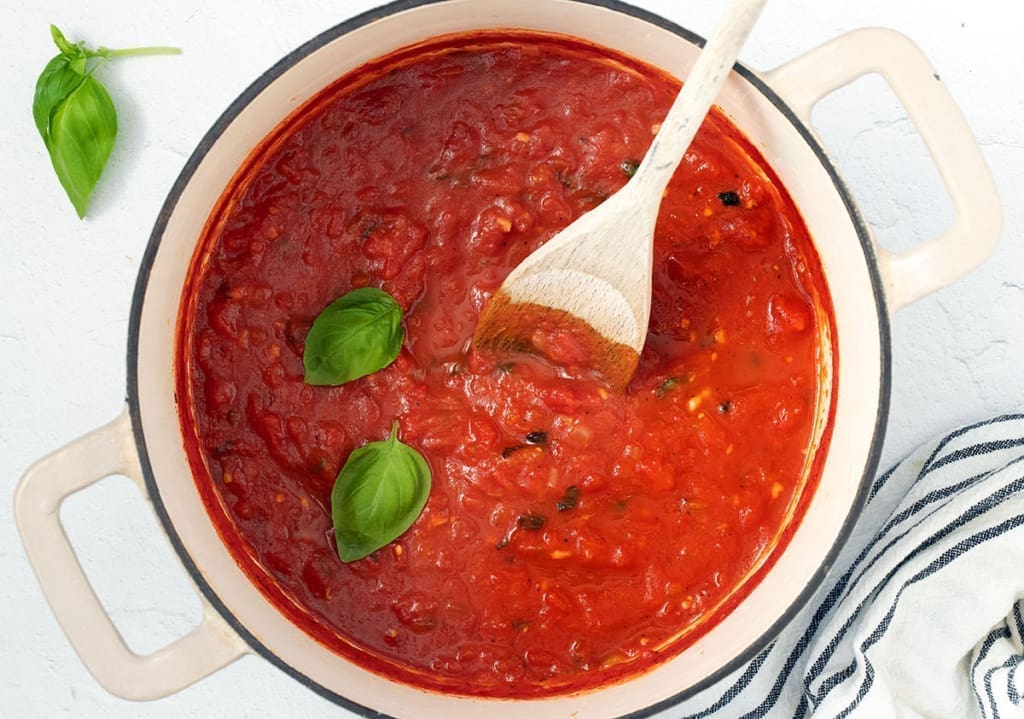 Sugo Sauce in a dutch oven with a wooden spoon and fresh basil.