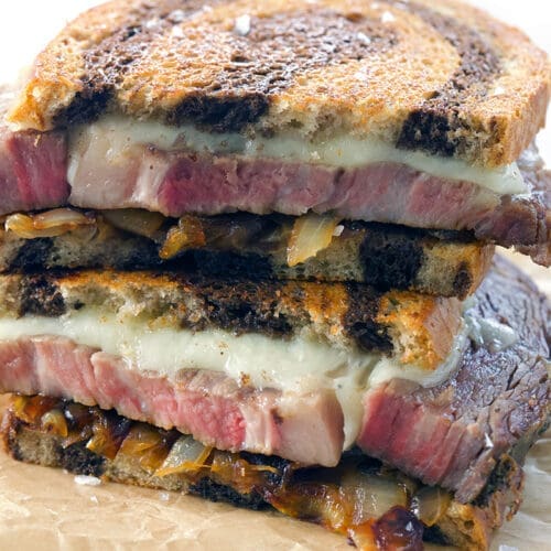 Prime rib patty melt cut in half on parchment paper.