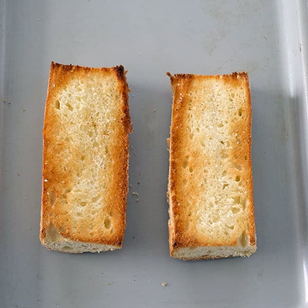 Two pieces of garlic bread on a silver baking sheet.