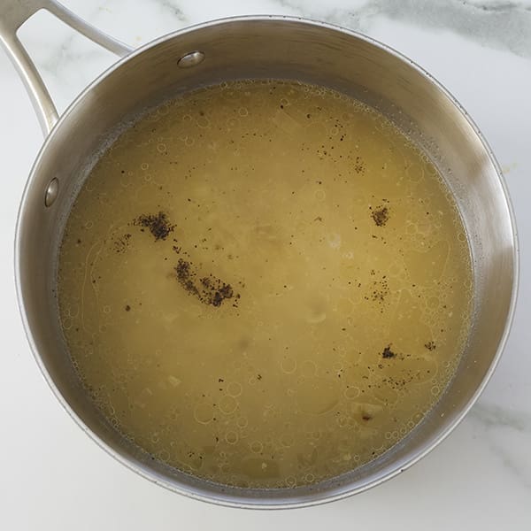 Silver saucepan with yellow liquid inside.