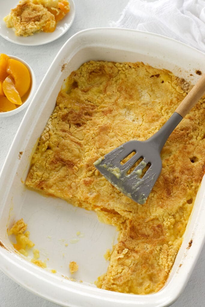White pan of peach dump cake with piece missing.