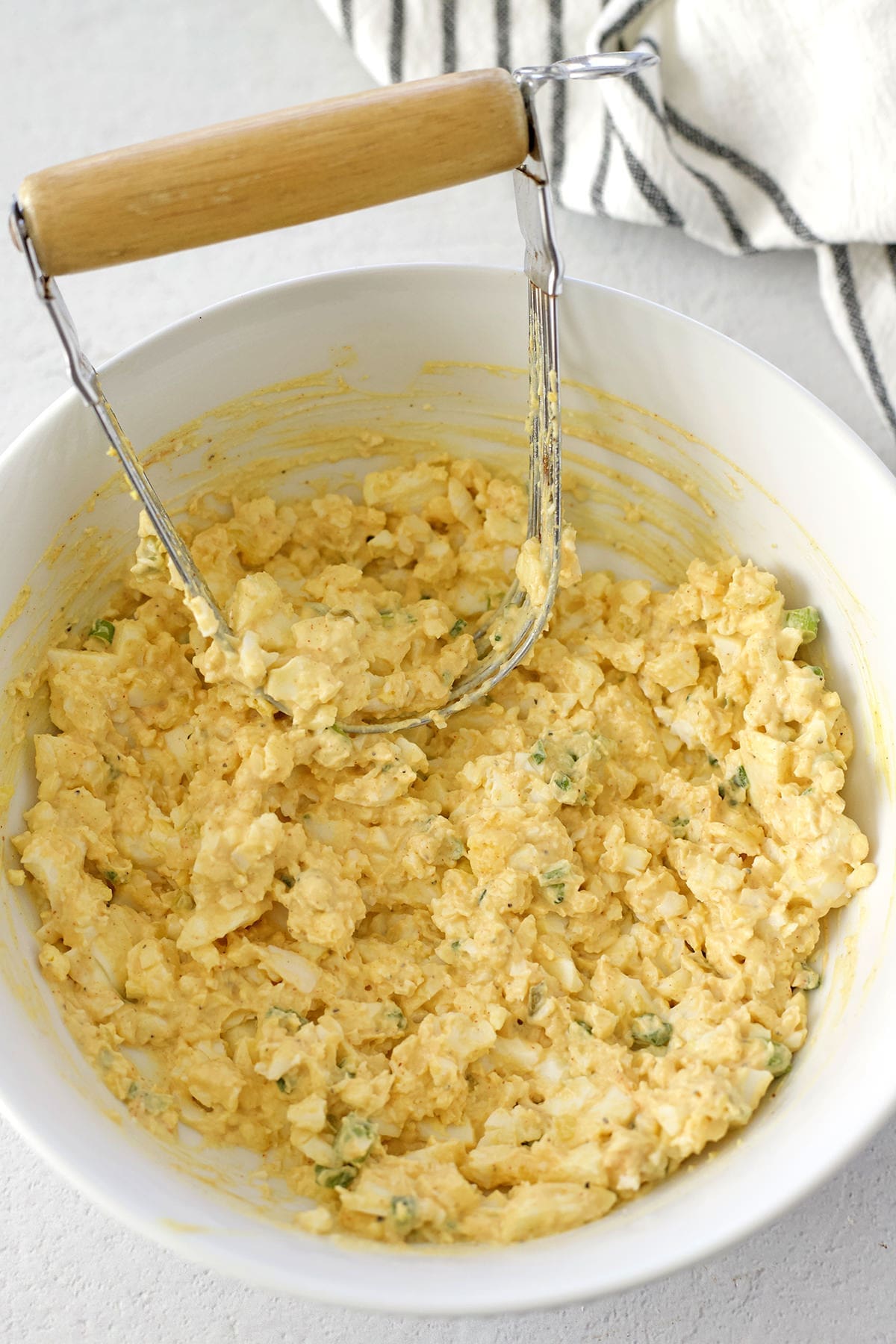 White bowl with mashed hard boiled eggs and a pastry cutter.