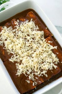 Unbaked beef enchiladas topped with shredded cheese.