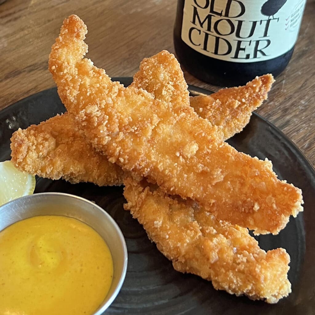 Black Plate with 3 strips of Plaice Goujons with a side of mustard.