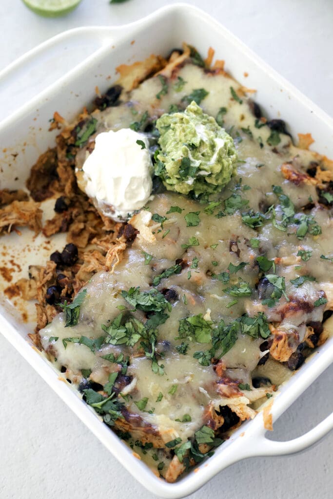 Baked chicken enchilada casserole topped with sour cream with one serving removed.